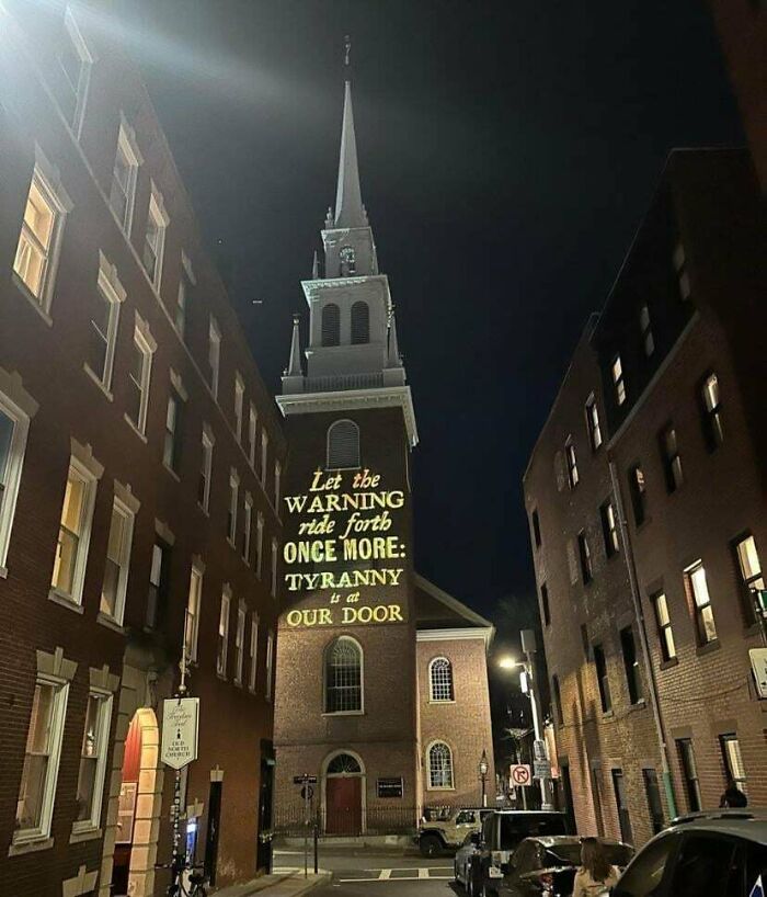 Church steeple at night with a chaotic good message about tyranny projected on the building in an urban street setting.