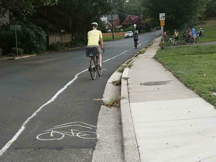 Cyclist riding on a street with a chaotic good painted bike lane symbol leading into the curb edge on a quiet neighborhood road.