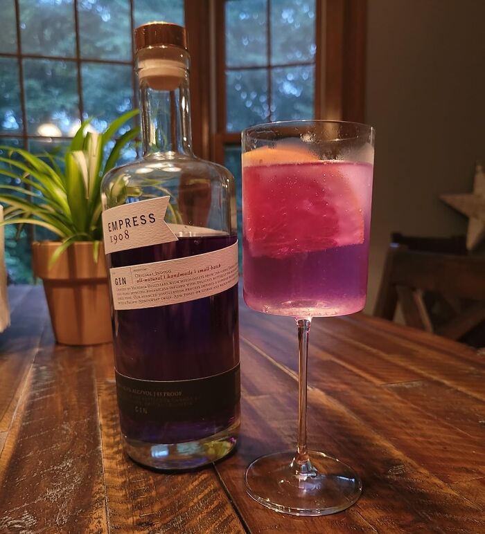 Bottle of Empress 1908 gin next to a purple cocktail with lemon slice, showcasing creative fancy lemonade drink ideas.