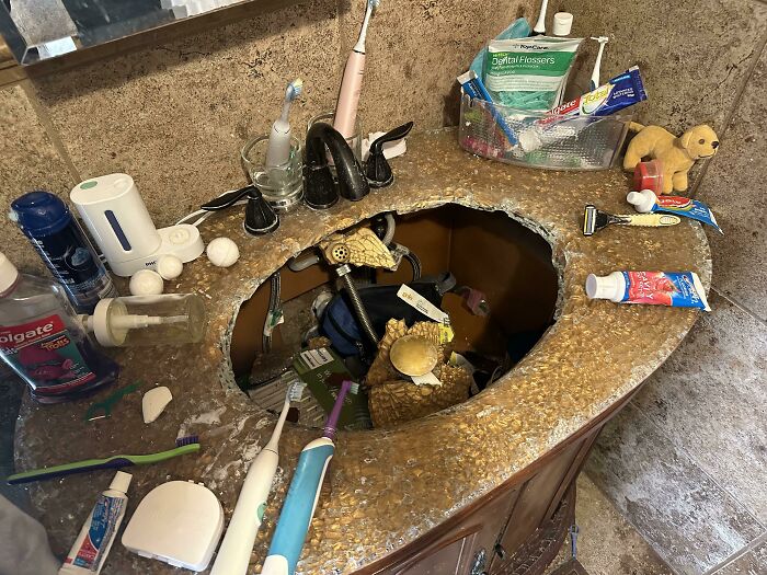Bathroom sink with a large hole and scattered toiletries, showing an unlucky parenting mishap at home.