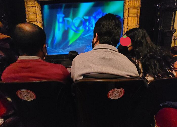 Three people from behind sitting in theater seats watching a Frozen stage show, reflecting moments of unlucky parents' outing.