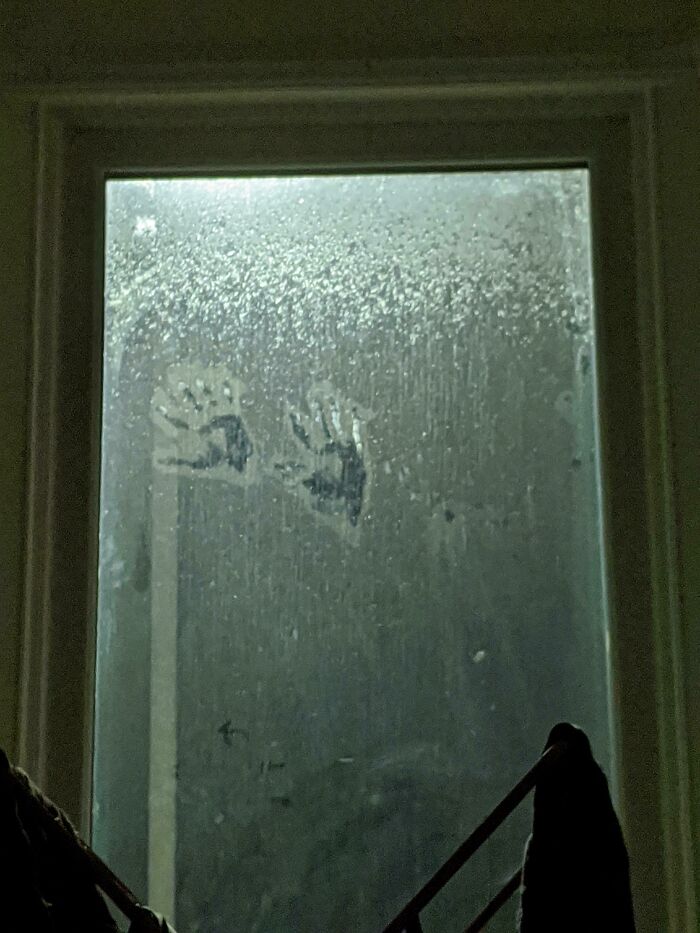 Faint handprints on a foggy window at night, suggesting eerie ghost encounters in a dark, misty setting.