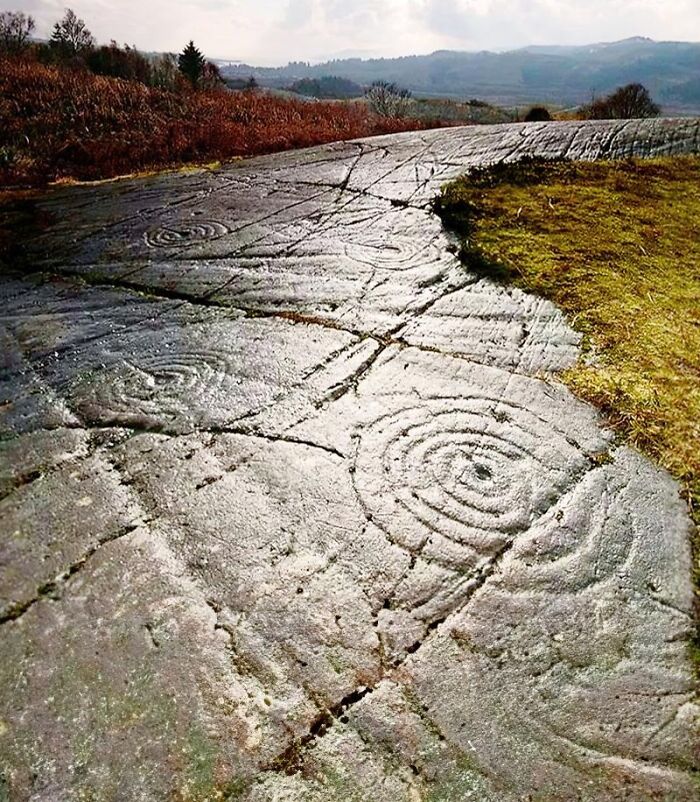 Ancient history stone carvings on a rocky surface with spiral patterns in an outdoor natural landscape.