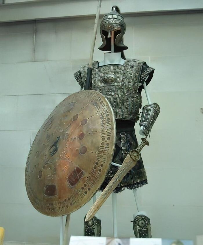 Ancient history warrior armor and shield displayed in a museum, showcasing detailed metal craftsmanship and design.