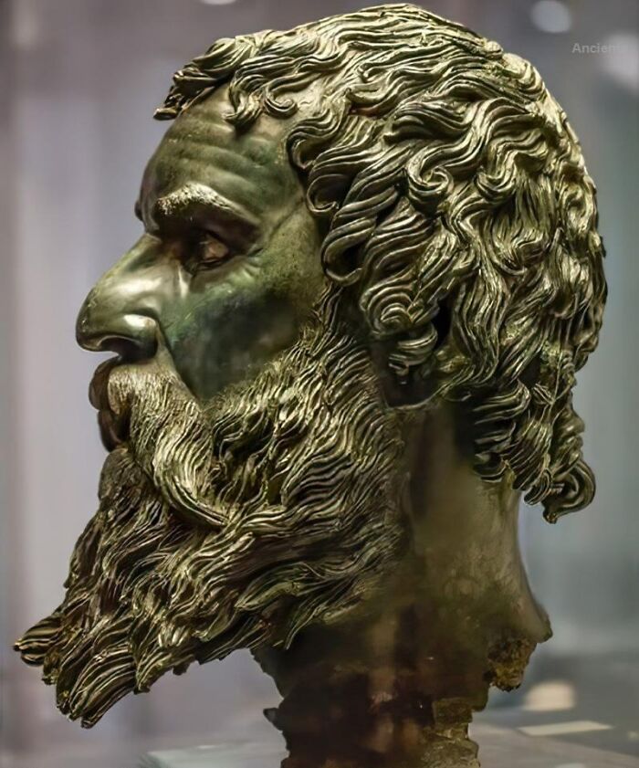 Bronze ancient history bust showing detailed hair and beard sculpture from an archaeological museum exhibit.