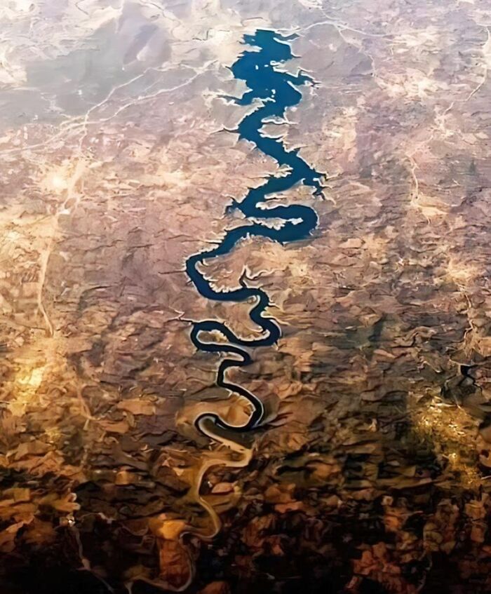 Aerial view of a winding river cutting through ancient history landscape with rugged terrain and arid surroundings.