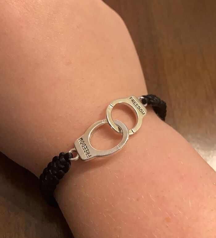 Linked silver handcuff charm bracelet with freedom engraving on woven black cord on a wrist, friendship gift idea.