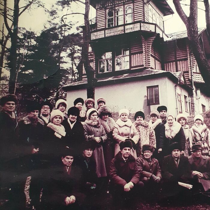 Group of people in winter clothing standing outside an old wooden house, evoking chilling ghost encounters atmosphere.