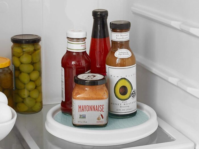 Condiments organized on a rotating tray inside a compact shoebox kitchen fridge to maximize space efficiently.