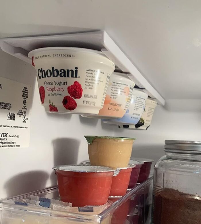 Yogurt containers neatly stored with a small kitchen solution rack, maximizing space in a cluttered fridge.