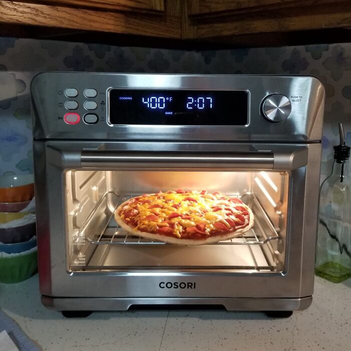 Compact stainless steel toaster oven baking pizza, showcasing small kitchen solutions for efficient use of cluttered spaces.