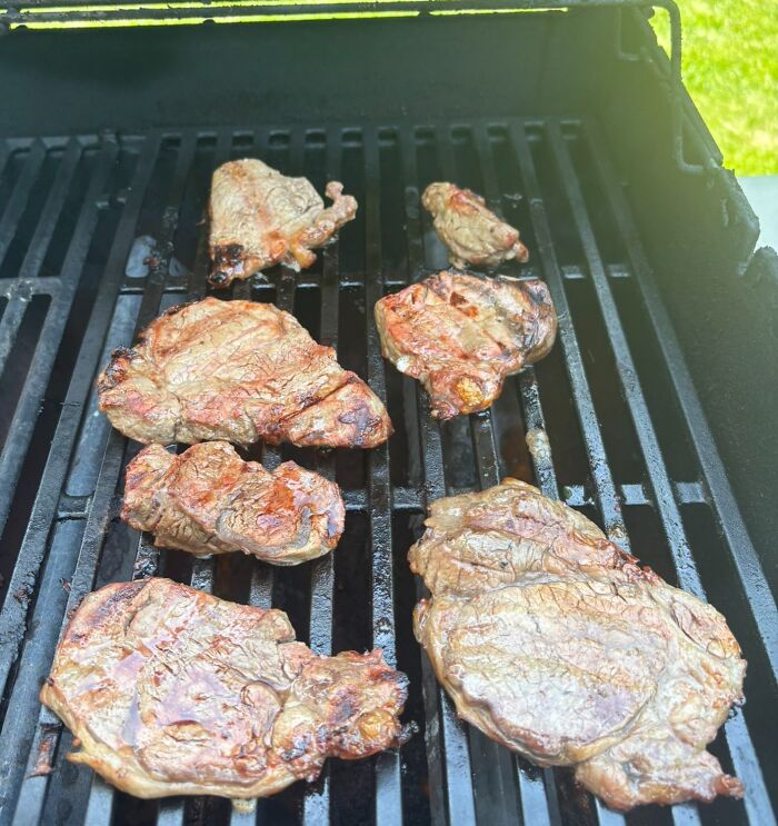 Grilled steaks on an outdoor barbecue representing a funny work-from-home meme about cooking during work breaks.