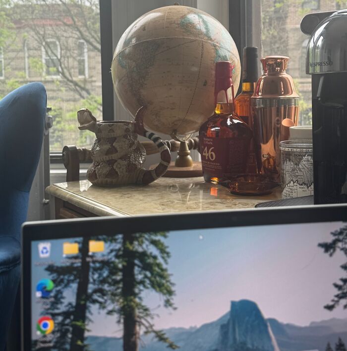 Work-from-home desk setup with laptop, globe, coffee machine, and decorative items by a window.
