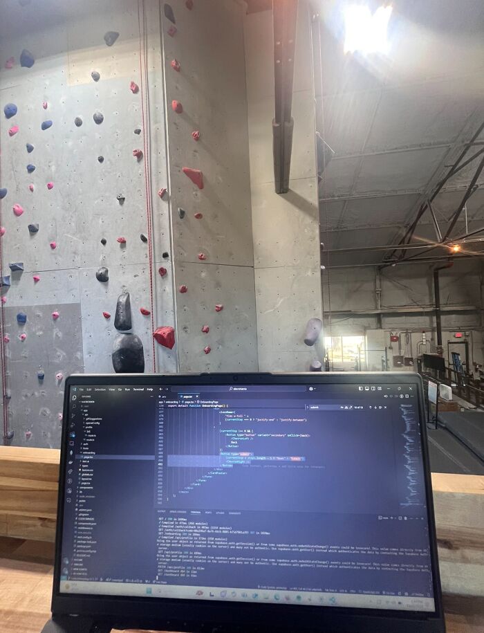 Laptop screen showing coding work in a spacious indoor climbing gym, illustrating funny work-from-home meme setup.