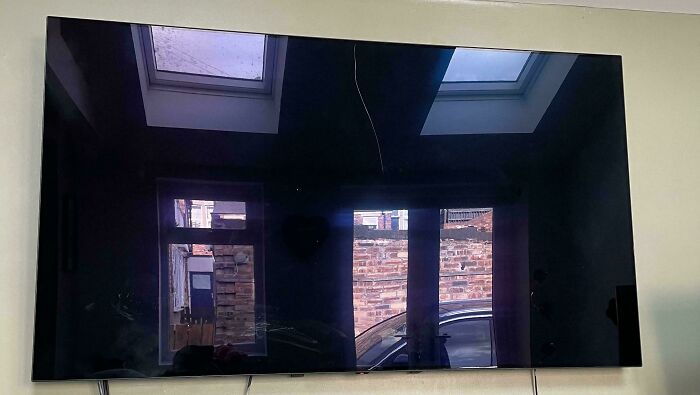A flat-screen TV mounted on a wall reflecting windows and a car outside, showcasing an unlucky parents' home moment.