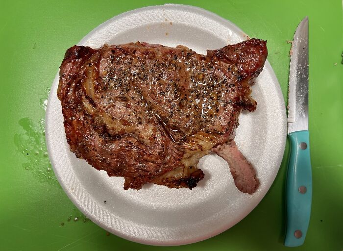 Grilled steak shaped like a pig on a white plate with a knife on a green cutting board, an interesting thing to double take.