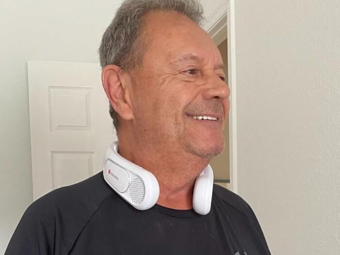 Man wearing a black shirt and a white neck speaker, smiling indoors, a perfect Father's Day gift idea.