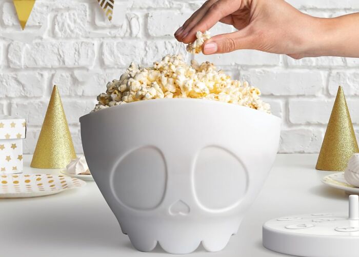 Hand picking popcorn from a skull-shaped bowl, perfect unique Father's Day gifts for popcorn lovers and fun celebrations.
