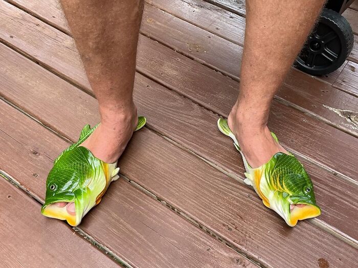 Novel fish-shaped slippers worn on feet, a quirky and fun Father's Day gift idea on wooden deck floor.