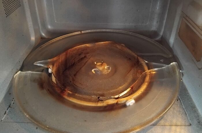 Broken microwave glass turntable plate burned inside, illustrating Friday the 13th mishap needing someone to hold their beer.