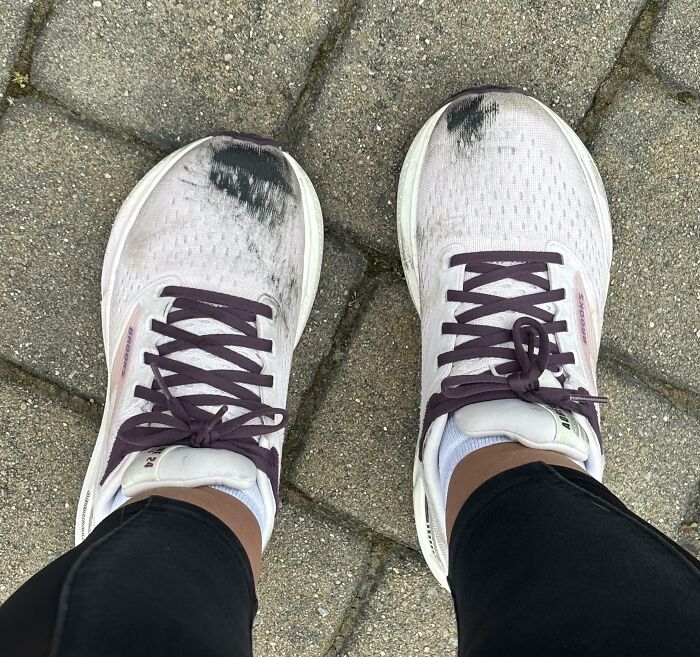 Worn white sneakers with purple laces on a stone pavement, showing dirt and wear after a tough Friday the 13th.