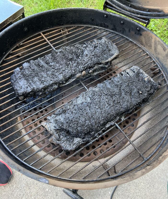 Two severely burnt ribs on a charcoal grill, illustrating a Friday the 13th cooking disaster.