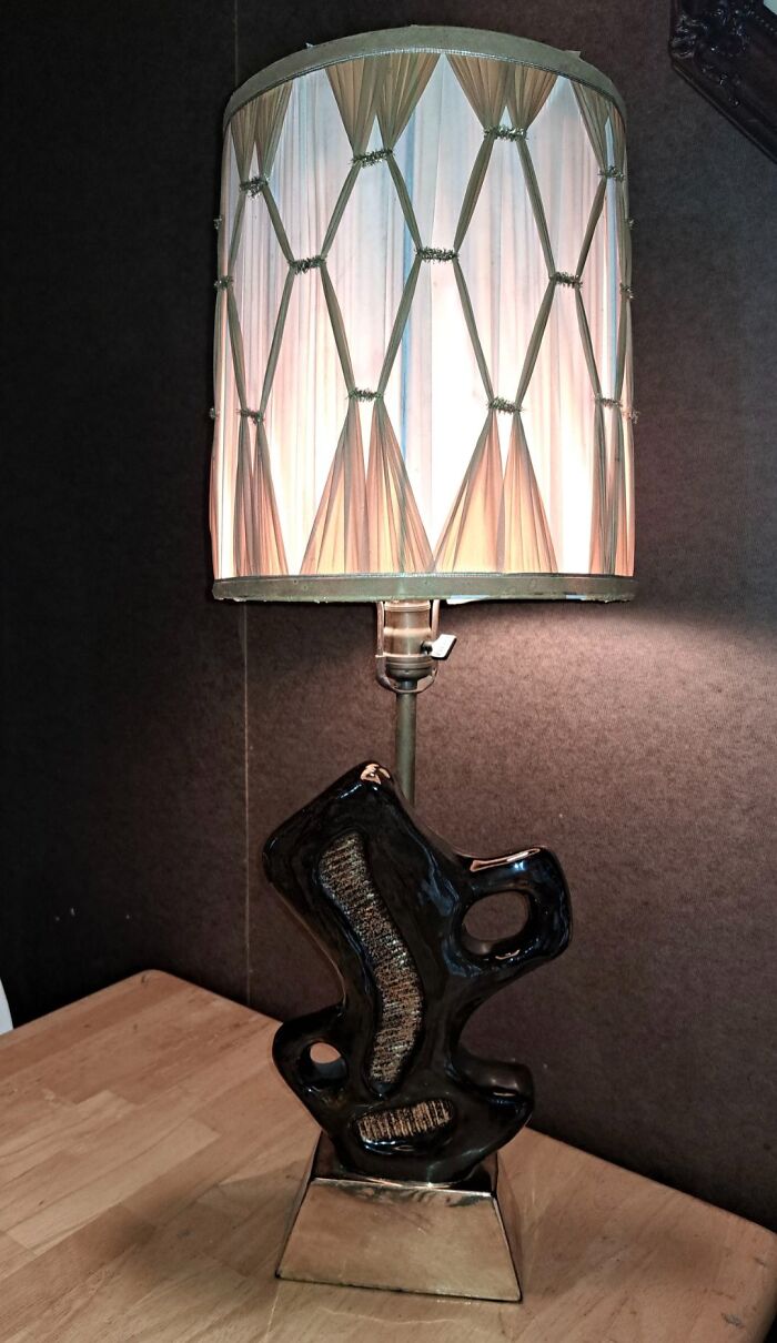 Vintage ceramic table lamp with unique sculptural base and pleated fabric shade, thrifted find in a cozy setting.
