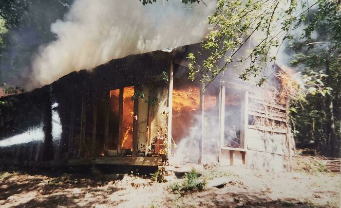 Old wooden cabin engulfed in flames and smoke in a forest setting, evoking chilling ghost encounters atmosphere.