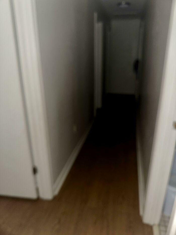 Dimly lit narrow hallway with wood floor and white walls, evoking chilling ghost encounters and eerie atmosphere.