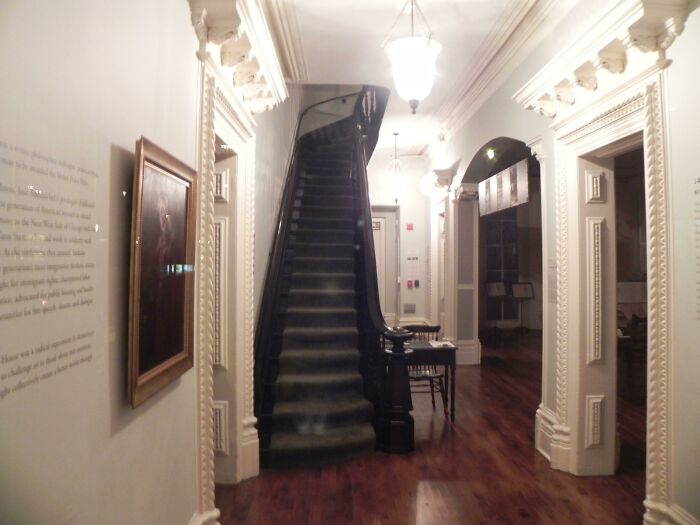 Dimly lit historic hallway with wooden floors and a black staircase, evoking chilling ghost encounters atmosphere.