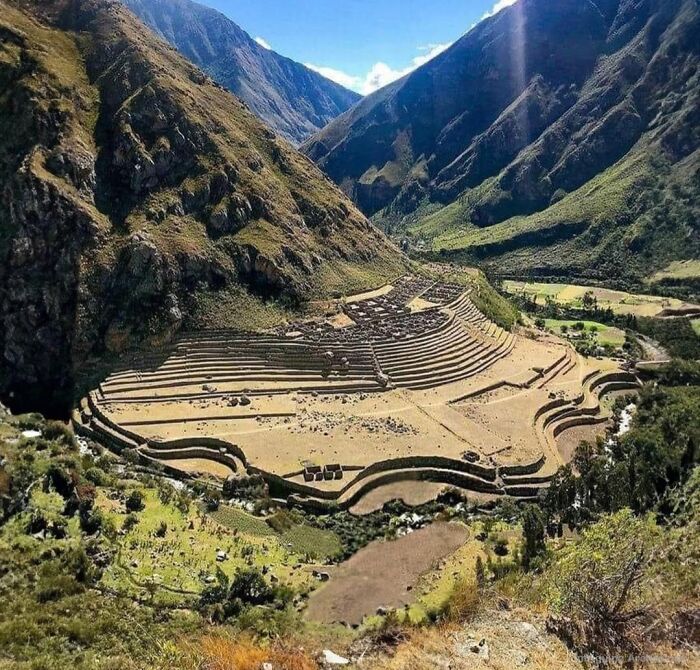 Terraced ancient history site nestled in a mountainous valley under clear skies, showcasing archaeological ruins and landscape.