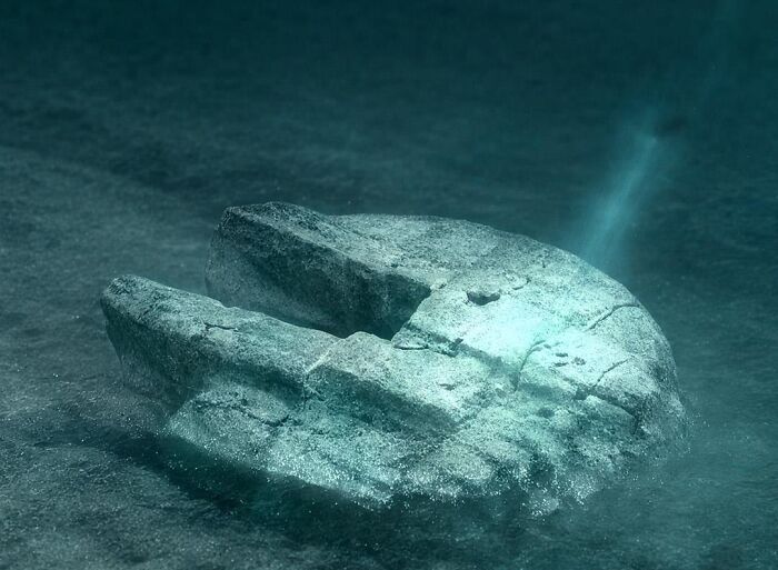 Underwater ancient stone artifact partially buried in sand, revealing details related to ancient history discoveries.