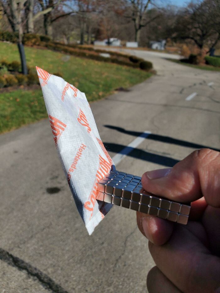 Hand holding small magnets gripping a silica gel packet outdoors, demonstrating a clever life hack for easy handling.