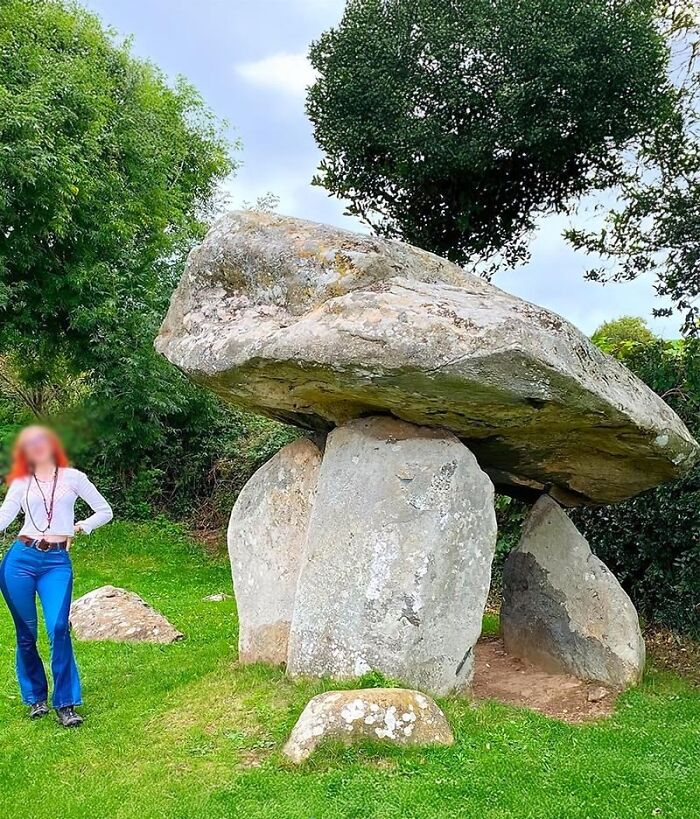 Ancient history stone monument surrounded by greenery with a person standing beside it on a grassy site.