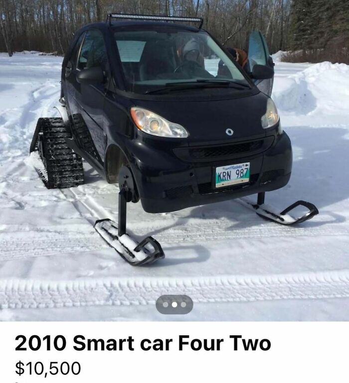 Black 2010 Smart car with snow tracks and skis, modified for winter terrain, spotted for sale in snowy landscape.