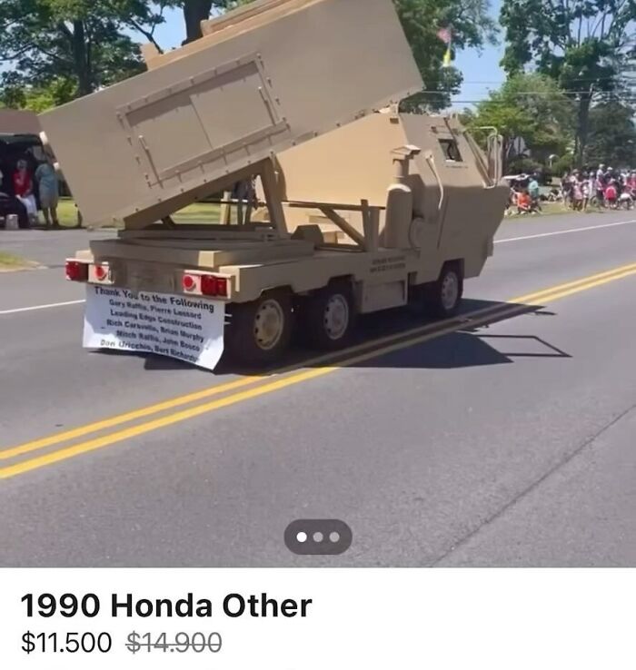 Six-wheeled beige utility vehicle with raised bed on a road during a public event, chaotic cars spotted for sale.