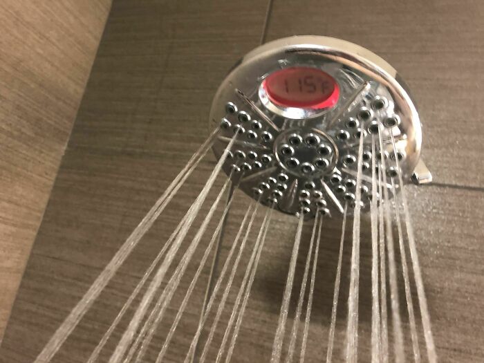Showerhead with water flowing and a temperature display, showcasing genius hotel design decisions in bathroom fixtures.