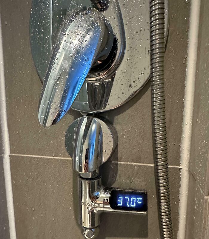 Modern hotel shower design with digital temperature display showing 37°C on chrome fixtures and water droplets on tiles.