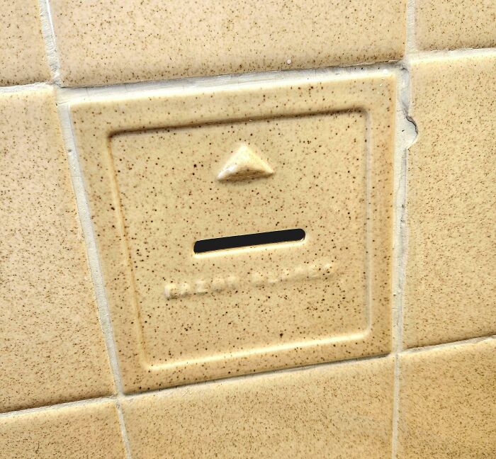 Unique hotel design decision featuring a hidden slot in speckled beige wall tiles for creative functionality.