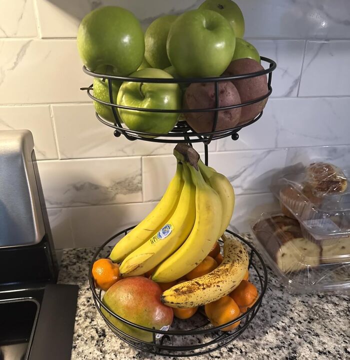 Two-tier fruit basket with bananas, green apples, mango, and oranges on a kitchen countertop for kitchen glow-up ideas.