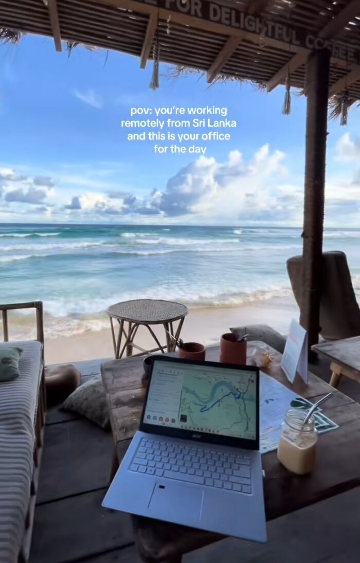 Laptop on a wooden table by the beach showing work-from-home setup with ocean view, embodying funny work-from-home memes.