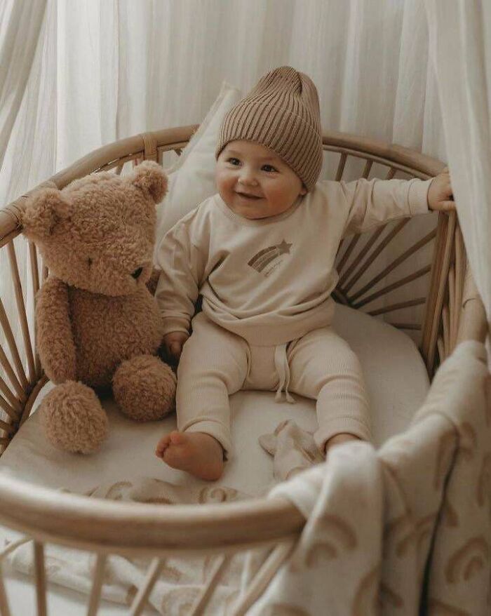 Baby sitting in a crib with a teddy bear, representing ways things have changed through the years according to people online.