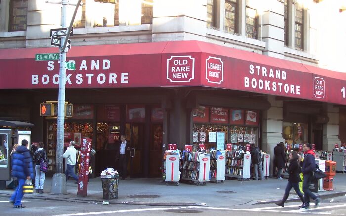 Strand Bookstore exterior with people browsing outdoor book displays, showcasing a grandiose and magical bookstore scene.