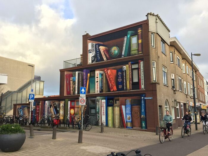 Building facade painted with giant books, creating a stunning and impressive bookstore and library street art scene.