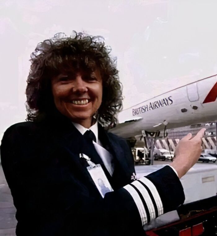 Female pilot in uniform smiling and pointing at a British Airways plane illustrating unusual and wonderful facts.