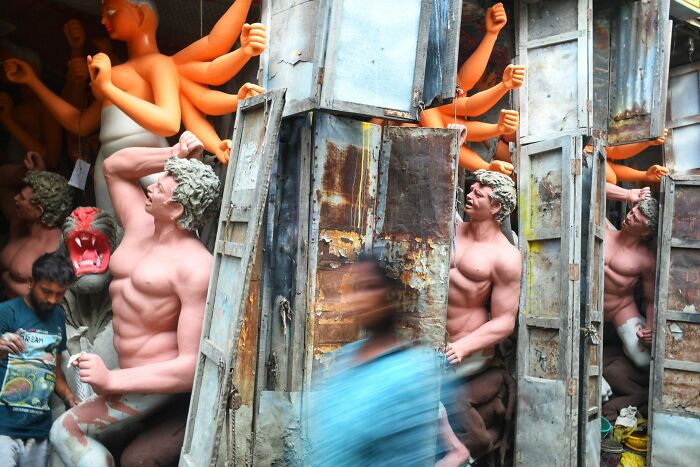 Blurred figure walking past large sculpted figures with arms raised in a vibrant urban scene, illustrating Pure Street Photography Grant.