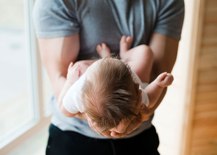 Man holding a newborn baby gently indoors by a window, illustrating themes of trauma and difficult relationships.