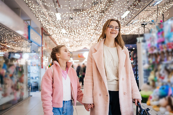 Woman and child holding hands in a shopping mall under decorative lights, illustrating kid outings and family interactions.