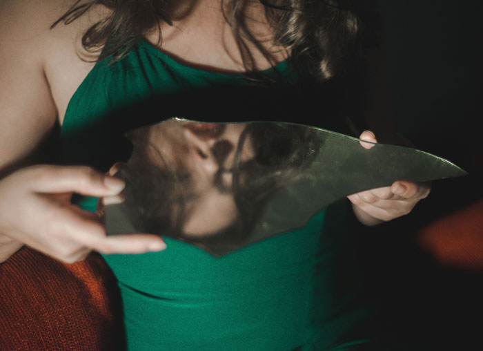 Woman in green dress holding a broken mirror reflecting her face, illustrating problematic behaviors women get a pass for