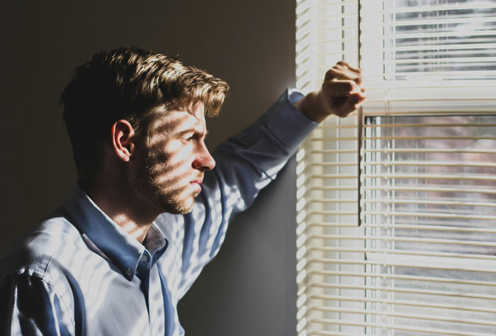 Man looking through window blinds with serious expression, reflecting on secrets spouses keep after marriage